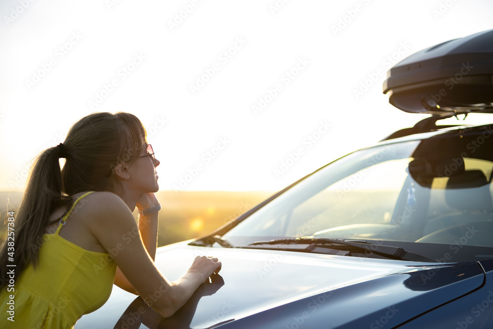 Naklejka premium Happy woman driver in summer dress enjoying warm evening near her car. Travel and vacation concept.