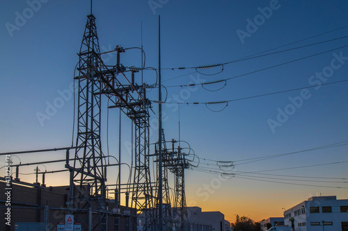 Industrial power substation at dusk with high voltage lines, pylons, and lightning arresters, orange and blue sunset, nobody 