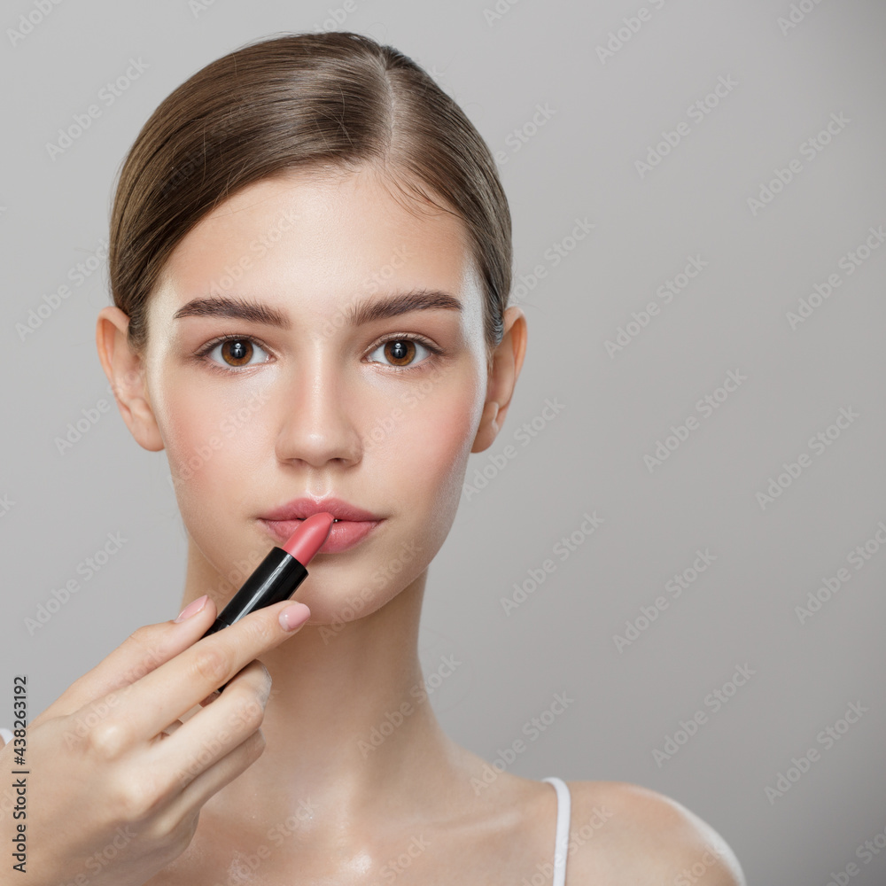 Beauty portrait. Beautiful girl paints lips with pink lipstick. Gray background. Beauty portrait. Beautiful girl paints lips with pink lipstick. Gray background.