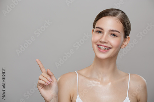 Lovely girl in braces smiling and pointing at the empty space