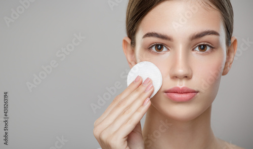 Beauty portrait. A pretty girl with clean skin holds a cotton pad. Gray background.