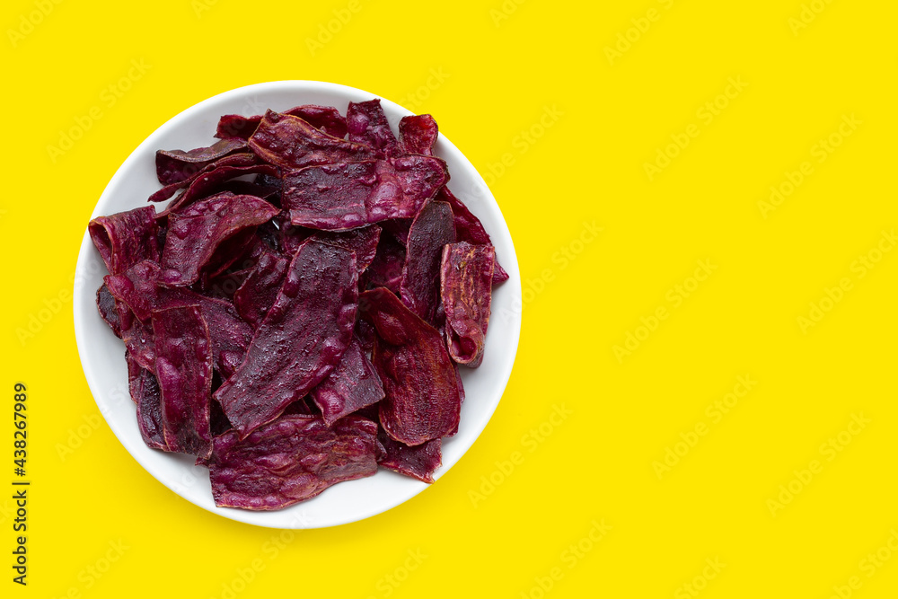 Obraz premium Purple sweet potato chips in white plate on yellow background.