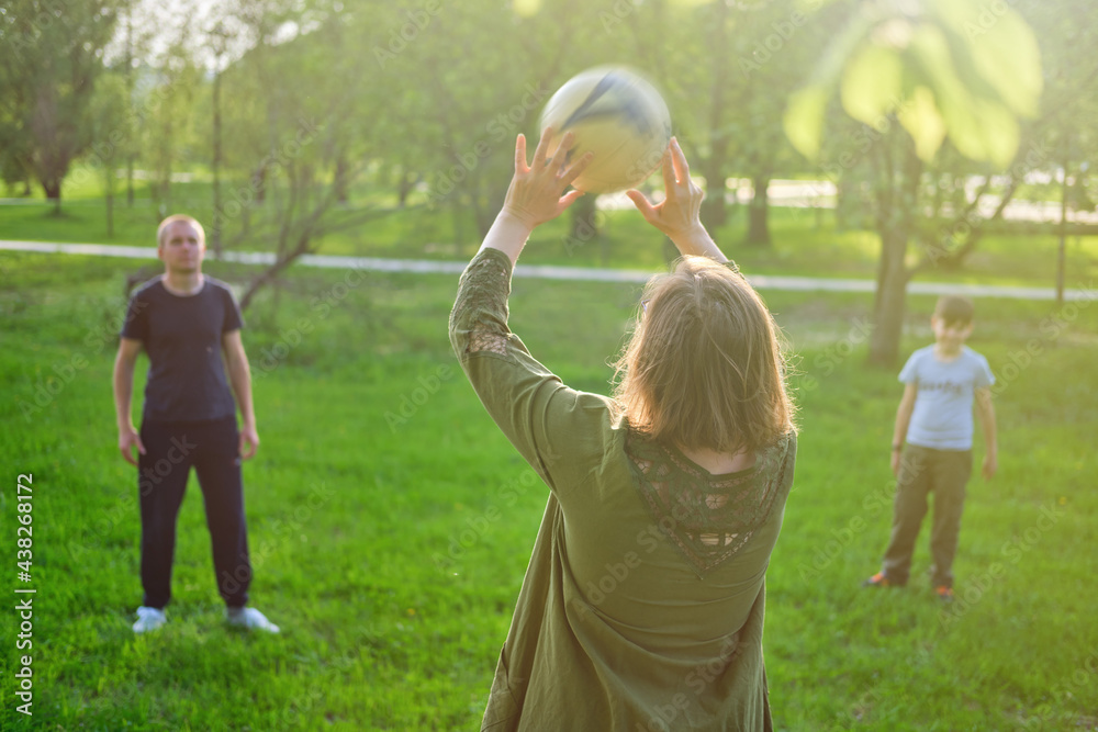 Mom, dad and son play ball in nature, park lawn with summer grass