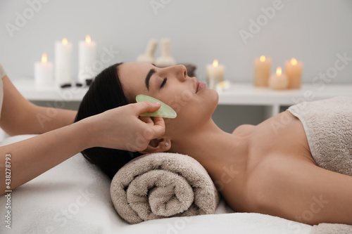 Young woman receiving facial massage with gua sha tool in beauty salon photo