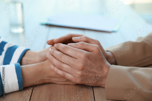 Psychotherapist holding patient s hands at table indoors  closeup