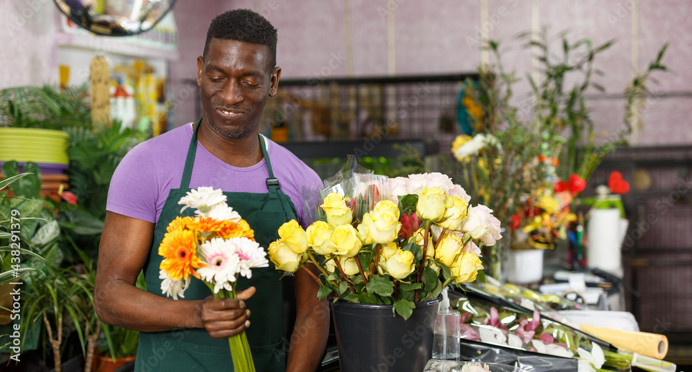 Portrait of successful African-American man owner of floral store standing with fresh flowers