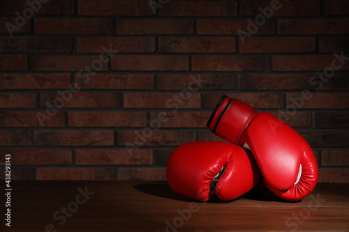 Pair of red boxing gloves on wooden table near brick wall © New Africa