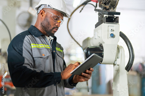 African mechanical engineer working for maintenance or repairing robotic welding machine in factory.