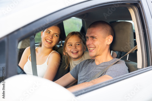 Positive family of three driving in the car with open windows, they talking and laughing