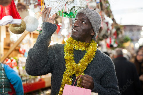 Afro-American guy in festive mood walking through street Christmas fair, choosing handmade decorations.