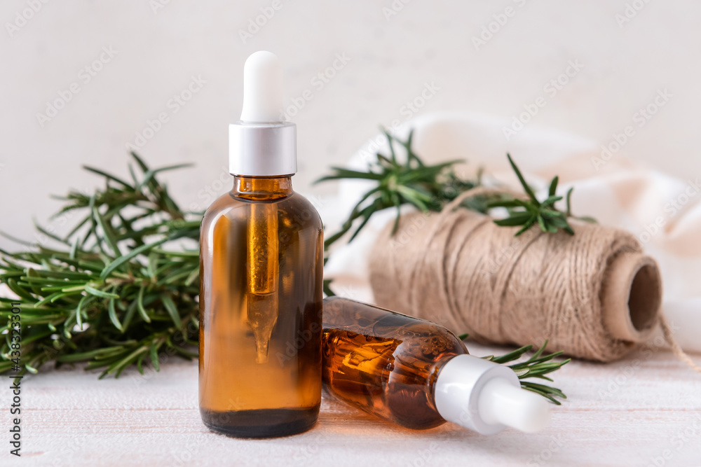 Bottles of essential oil, fresh rosemary and rope on light background Bottles of essential oil, fresh rosemary and rope on light background