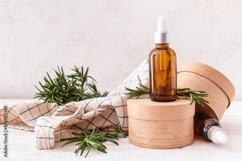 Composition with bottles of essential oil and fresh rosemary on light wooden background