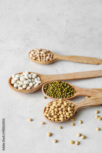 Spoons with different legumes on light background