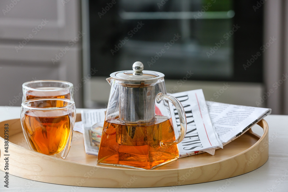 Teapot and cups of hot beverage on table in room
