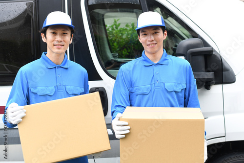 車の前で作業服を着た複数の男性が引っ越しの段ボールを運ぶイメージ © koumaru