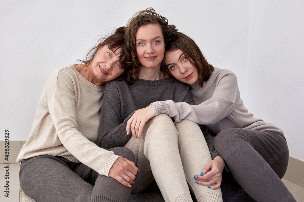 Group of smiling women of various ages wearing comfortable knitted sweaters and pants cuddling together and looking at camera