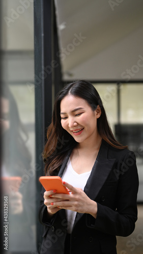 Portrait of happy businesswoman using smart phone while standing in office.