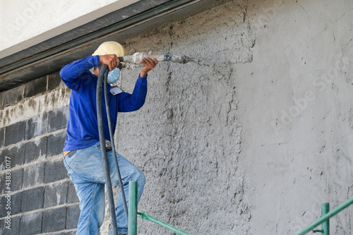 Plasterers using and operating sprayer mortar equipment machine for spraying mortar concrete cover brick wall and plastering for the decoration finishing work at the construction site
