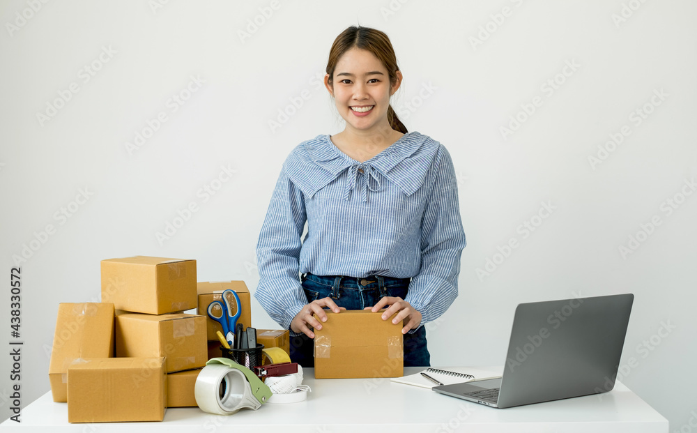Young Asian woman business owner with many parcel boxes on the table happy online sales job, use the laptop, get an order from customers, take notes, and make arrangements for delivery by post Young Asian woman business owner with many parcel boxes on the table happy online sales job, use the laptop, get an order from customers, take notes, and make arrangements for delivery by post