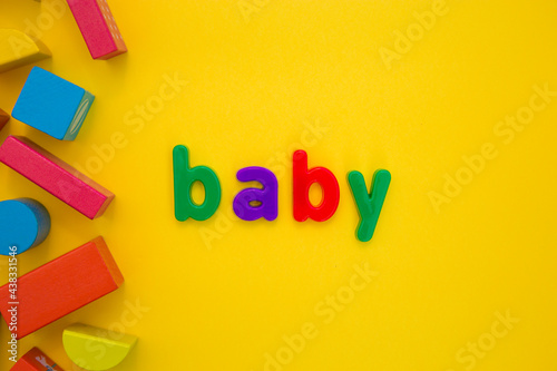 Kids Education, Creative, logical thinking concept. Colourful multicoloured building wooden toy blocks for children learning development word Baby from plastic letters on yellow background flat lay