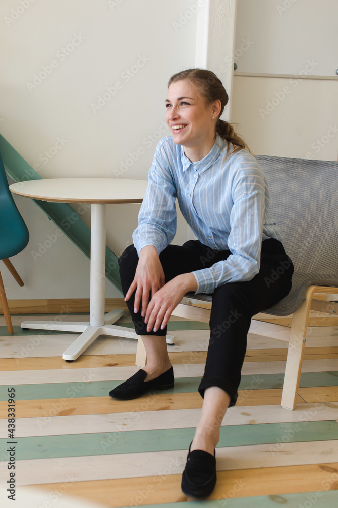 Full body of female worker laughing happily at spare time in modern workplace while looking away