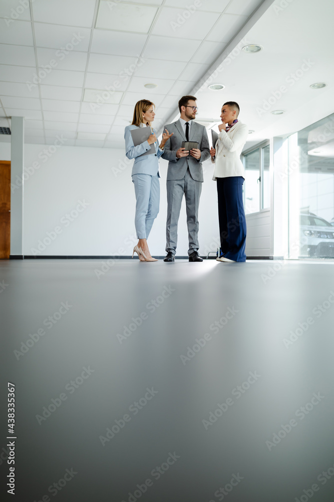 Business people in elegant clothes working together and smiling while standing in the office hallway Business people in elegant clothes working together and smiling while standing in the office hallway