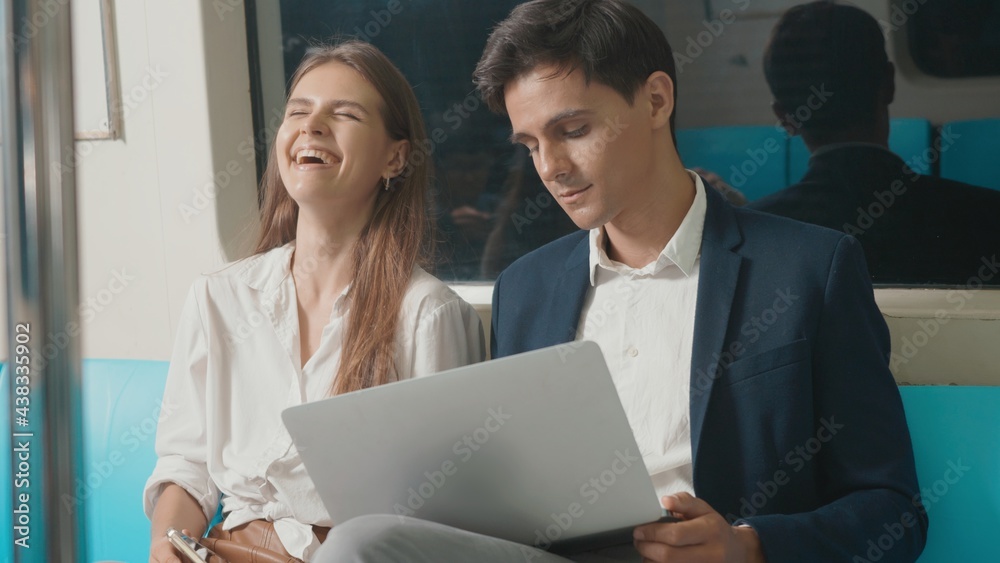 Young Caucasian white business woman and man sitting using laptop computer working talking together on the subway train in the morning during going to work, people transportation concept Young Caucasian white business woman and man sitting using laptop computer working talking together on the subway train in the morning during going to work, people transportation concept