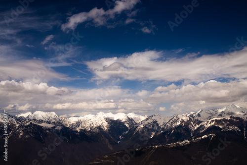 Landscape view of the tops of mountains covered in snow and blue sky with fluffy clouds.