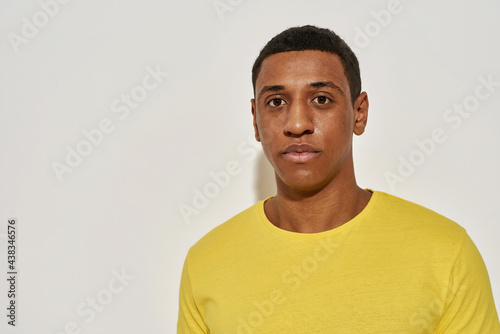 Portrait of calm young mixed race man in casual yellow t shirt looking at camera while posing isolated over gray background