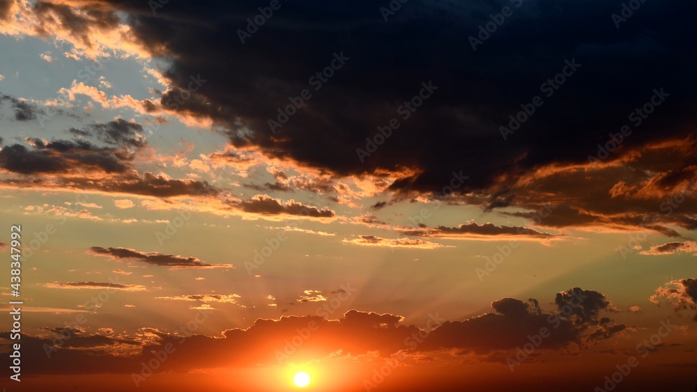 Obraz premium Shiny golden sun rays break through dark clouds. Orange color cloudscape of sunset. Dramatic sky while sundown in dusk