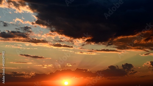 Shiny golden sun rays break through dark clouds. Orange color cloudscape of sunset. Dramatic sky while sundown in dusk © Ninel