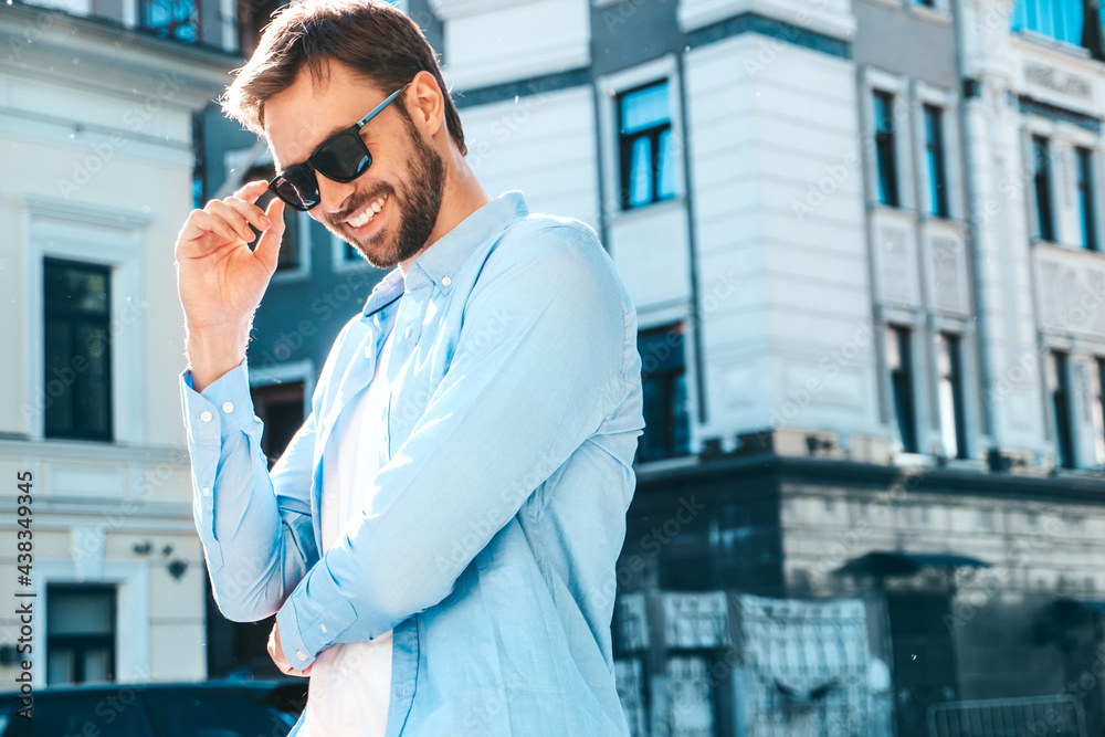 Portrait of handsome smiling stylish hipster lambersexual model.Modern man dressed in blue shirt. Fashion male posing near skyscraper on the street background in sunglasses. Outdoors at sunset Portrait of handsome smiling stylish hipster lambersexual model.Modern man dressed in blue shirt. Fashion male posing near skyscraper on the street background in sunglasses. Outdoors at sunset