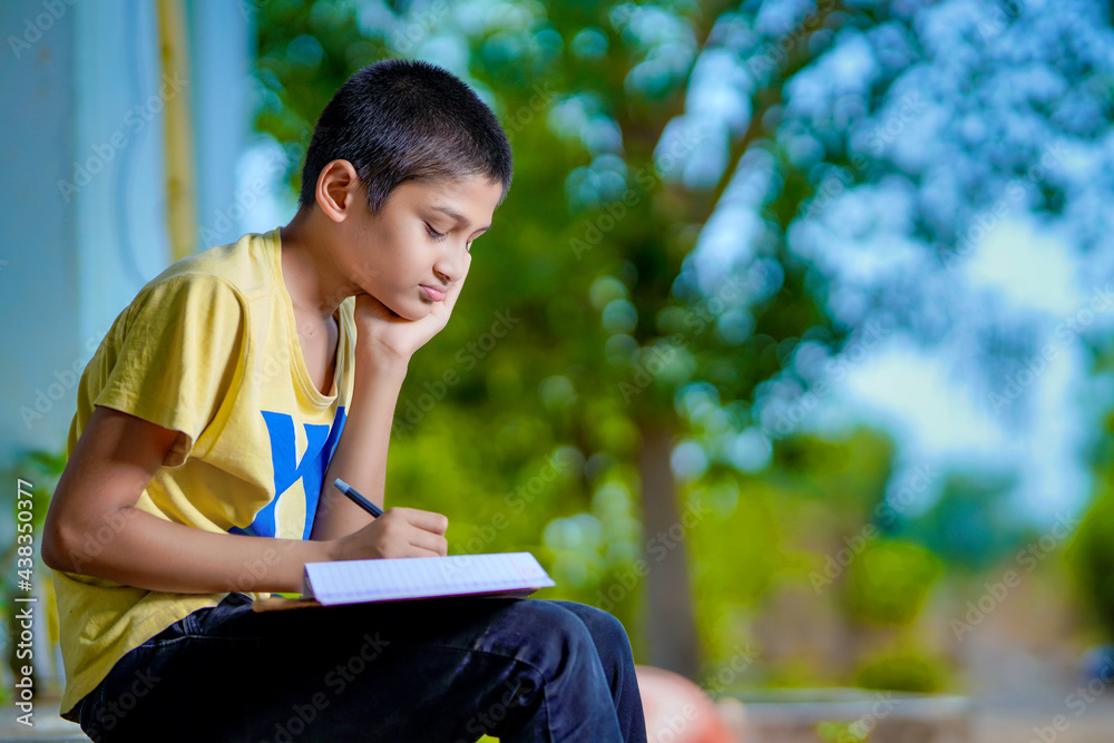 Fototapeta premium Indian school boy holding phone distance learning class using mobile application, watching online lesson, video calling in app making notes studying at home