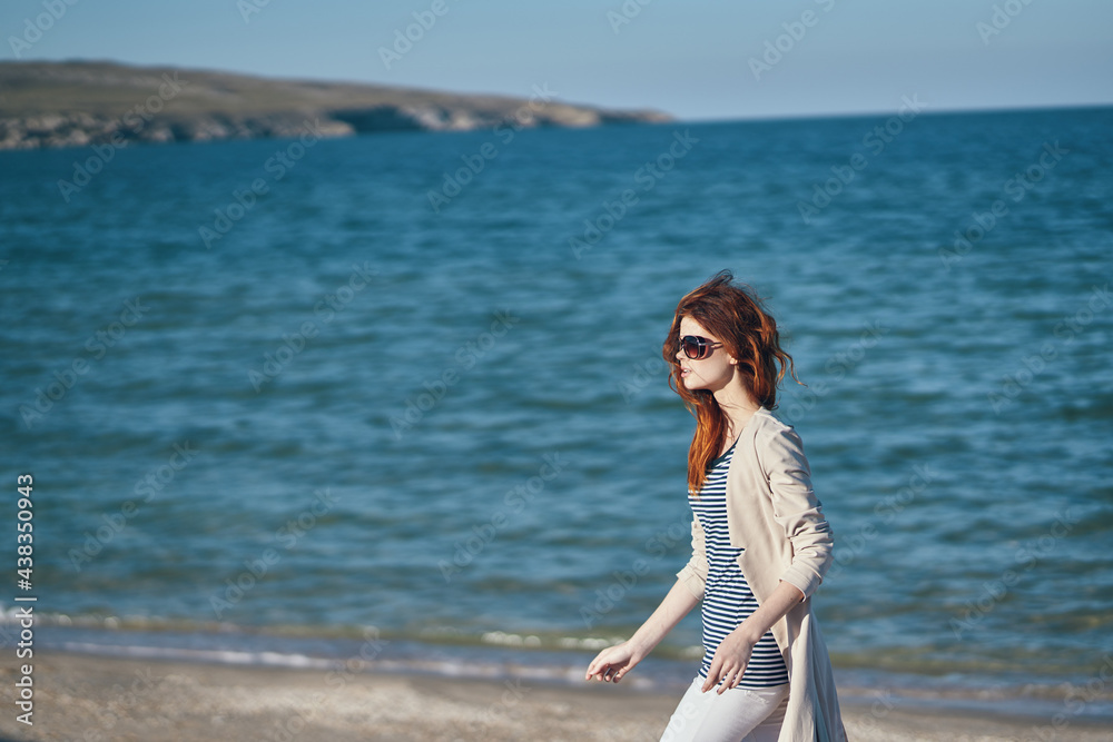 woman in sunglasses and trousers walking along the beach near the sea in the mountains woman in sunglasses and trousers walking along the beach near the sea in the mountains