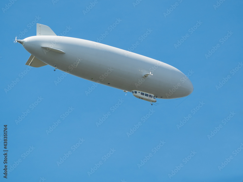 Obraz premium Cigar-shaped gray airship flies high in clear blue sky