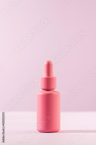 A mockup of a pink dropper with a facial serum on a pink background. Trends in facial skin care. Copy space.