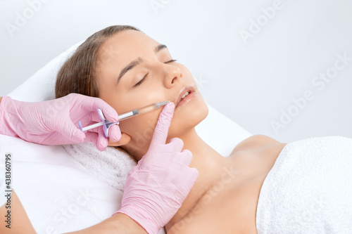 Cosmetologist does injections for lips augmentation and anti wrinkle in the nasolabial folds of a beautiful woman. Women's cosmetology in the beauty salon.