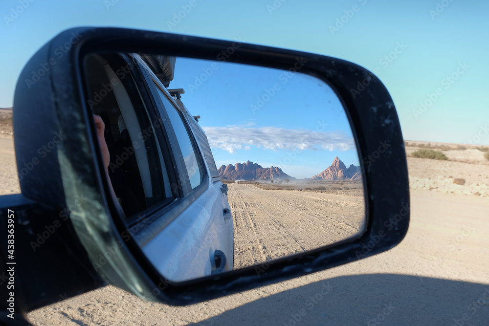 Views through the rear view mirror of a car of the Spitzkoppe Mountains in Namibia on a gravel road trip
