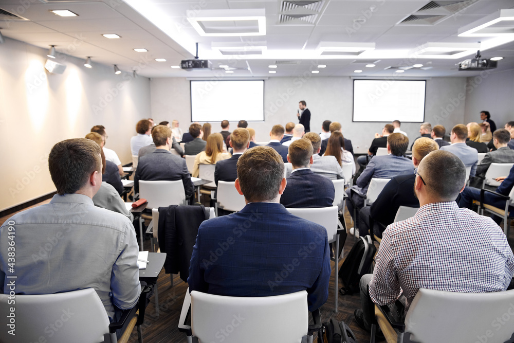 Group of people at the business conference, back view. Row of business people listen to the speaker on the forum or at seminar in modern conference room.
