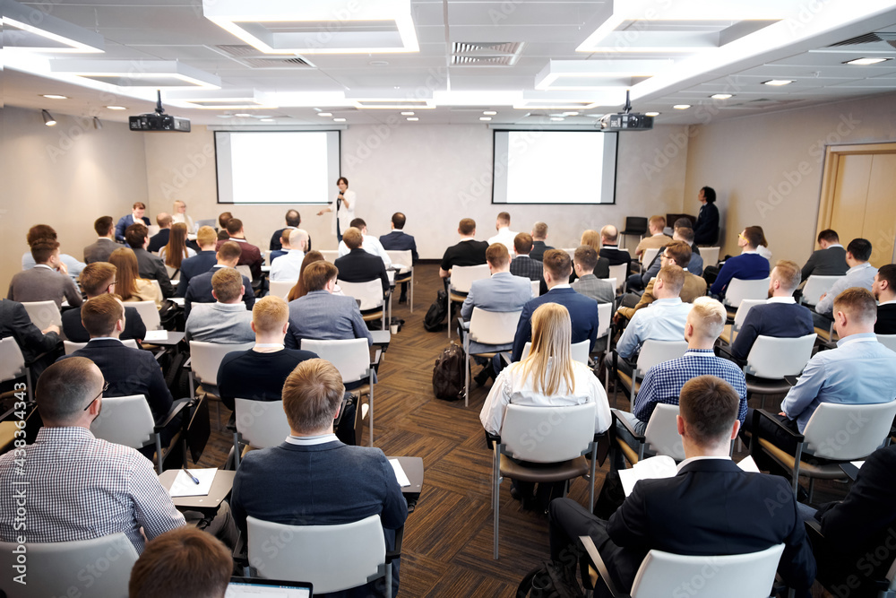 Fototapeta premium Group of people at the business conference, back view. Row of business people listen to the speaker on the forum or at seminar in modern conference room.