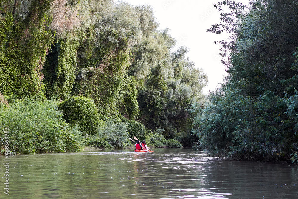 Couple kayaking on river together with green trees in the backgrounds. Having fun in leisure activity. Woman and man on the kayak. Sport, relations concept.