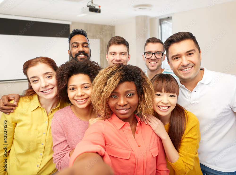 diversity, education and school concept - group of smiling international university students and teacher taking selfie over lecture hall on background