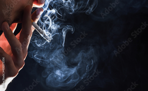Smoke and choke. Cigarette smoke dark background. Steaming cigarette in male hand.