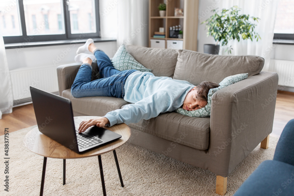 people, boredom and depression concept - bored or lazy young man with laptop computer lying on sofa at home