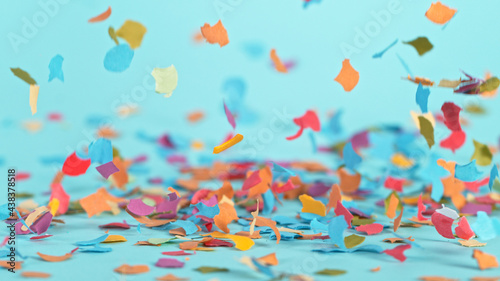 Color confetti falling on pastel blue background, macro shot.