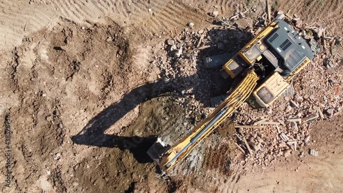 Excavator working on a construction site. Yellow excavator loading a truck on field. Building demolition. Digger cleaning ruins. 