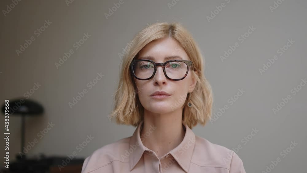 Blonde woman portrait in eyeglasses with a tense and sad emotions. Attractive stylish adult person looking at the camera with neutral expression. Concept of poker face