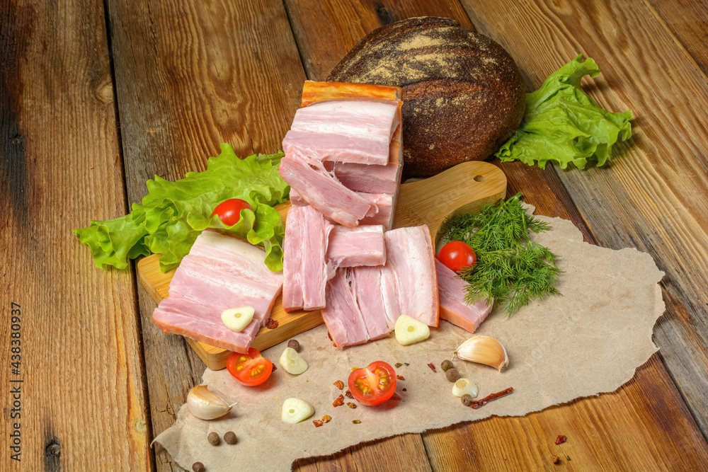 Smoked sliced pork belly, bacon, ham with herbs, tomatoes and black pepper on food paper. Wooden rustic background.Selective focus. Smoked sliced pork belly, bacon, ham with herbs, tomatoes and black pepper on food paper. Wooden rustic background.Selective focus.