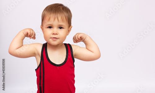 Obraz na płótnie little strong boy showing his biceps, gray background copy space
