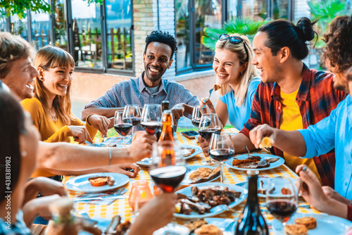 Group of friends having fun at bbq dinner outdoor in garden restaurant - Multiracial people eating food at barbecue backyard home party - Friendship, youth and party concept